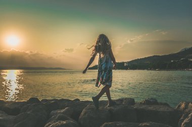 Gün batımında deniz kenarında dans eden sevimli kız.