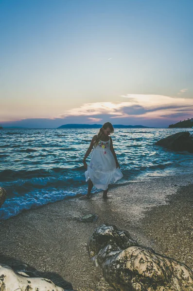 長い白いドレスを着た可愛い女の子日没時に海の水の中を歩く青いトーン効果 — ストック写真
