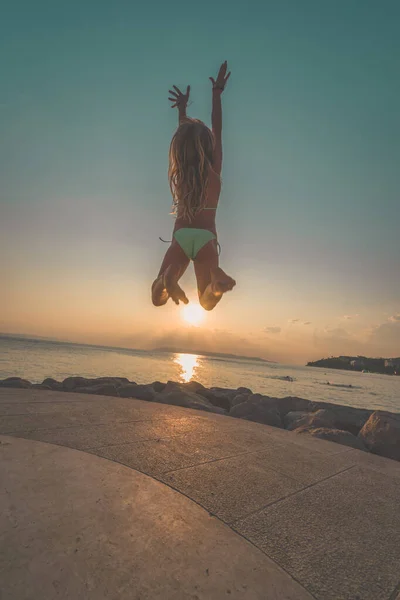 adorable girl in bikini jumping up at the sunset by the sea