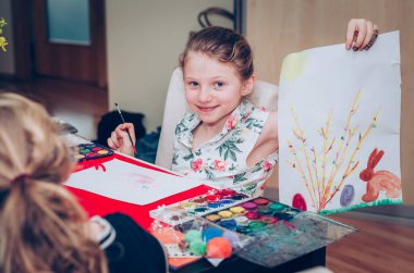 Sevimli sarışın kız masada oturuyor ve Paskalya teknesi yapıyor. 