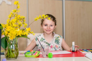 Sevimli sarışın kız masada oturuyor ve Paskalya teknesi yapıyor. 