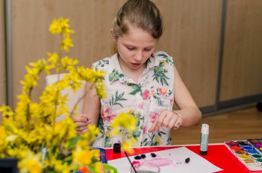 Sevimli sarışın kız masada oturuyor ve Paskalya teknesi yapıyor. 