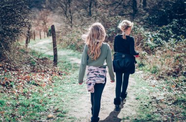 Sarı saçlı iki kız parkta arka planda yürüyor.