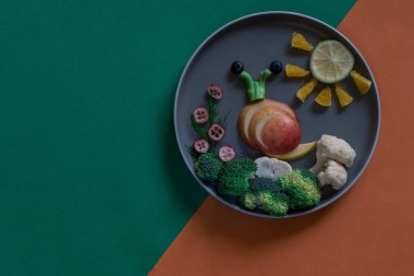 Tabaktaki yeşil ve turuncu arkaplanlı renkli sebzelerden salyangoz ve güneş şekli, boşluğu kopyala