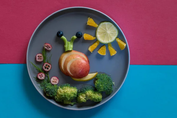 青と赤の背景を持つプレート上のカラフルな野菜からカタツムリと太陽の形 コピースペース — ストック写真