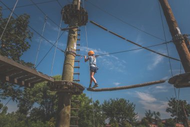 İp atlama parkında mavi arka planda ipe tırmanan çocuk.