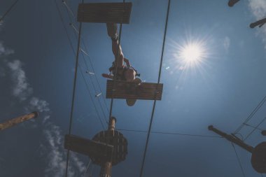 Cesur çocuk atraksiyon parkında ipe tırmanıyor. Profesyonel halat inşaatında. Açık havada, açık yaz gününde.