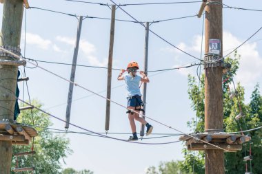 Korumalı miğfer ve emniyet kemeri takan cesur kız halata tırmanıyor. Halat atlama parkında. Açık havada güzel bir yaz günü.