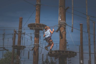 İp atlama parkında ipe tırmanan çocuk mavi gökyüzü ve günışığı arka planda