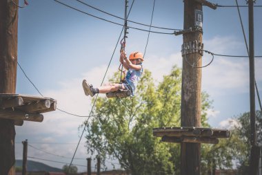 Korumalı miğfer ve emniyet kemeri takan cesur kız halata tırmanıyor. Halat atlama parkında. Açık havada güzel bir yaz günü.