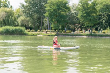 Kırmızı, güvenli, şişme yelek giyen çocuk sıcak yaz gününde kürek çekerek suyun üzerinde kürek çekiyor.
