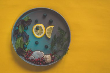 Limon dilimlerinden balık ve karnıbaharından deniz ve tabakta yaban mersini, sarı üzerine izole edilmiş kopya alanı.