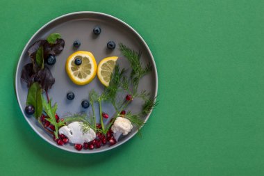 Limon dilimlerinden balık ve karnabaharından deniz ve tabakta yaban mersini, yeşil arka planda izole edilmiş kopya alanı