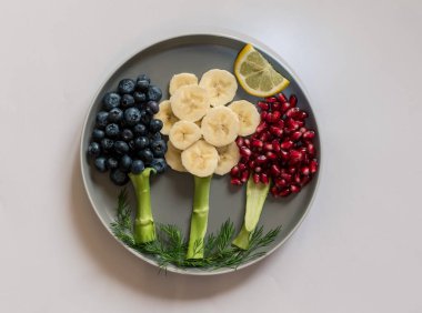 Tabakta muz, yaban mersini ve beyaz arka planda izole edilmiş nar elmalarından yapılmış meyve ağaçları var.