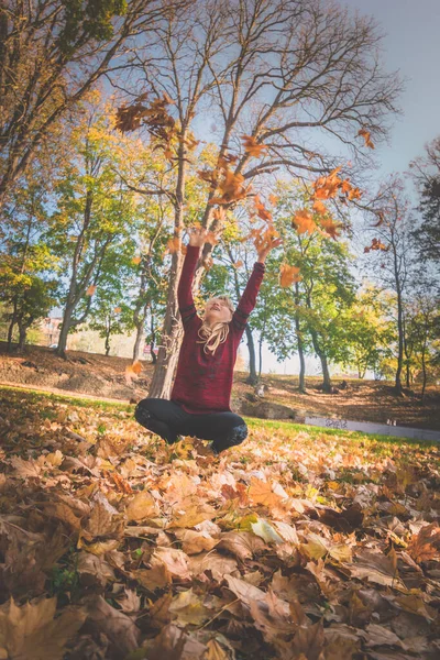 快乐的女孩坐在秋天的公园里 扔着五彩缤纷的树叶 — 图库照片