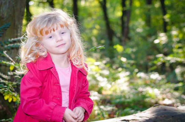 Blond girl in red coat in green forrest — Stock Photo, Image