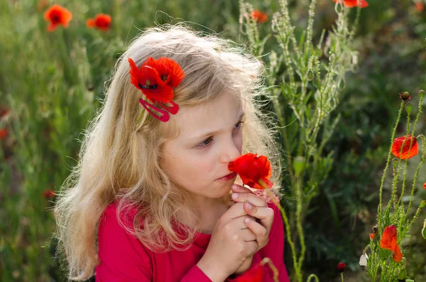 Blond girl smelling poppy flowers — Stock Photo, Image