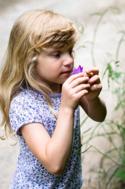 adorable blond girl smelling pink flower
