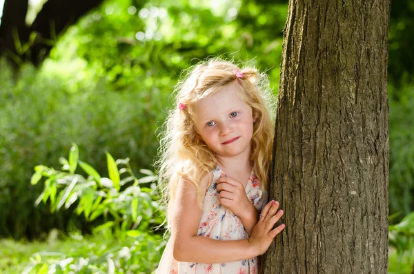 金发小女孩微笑着靠在树上 — 图库照片