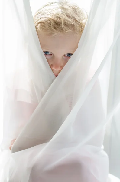 Eyes of little blond girl hiden by curtain — Stock Photo, Image