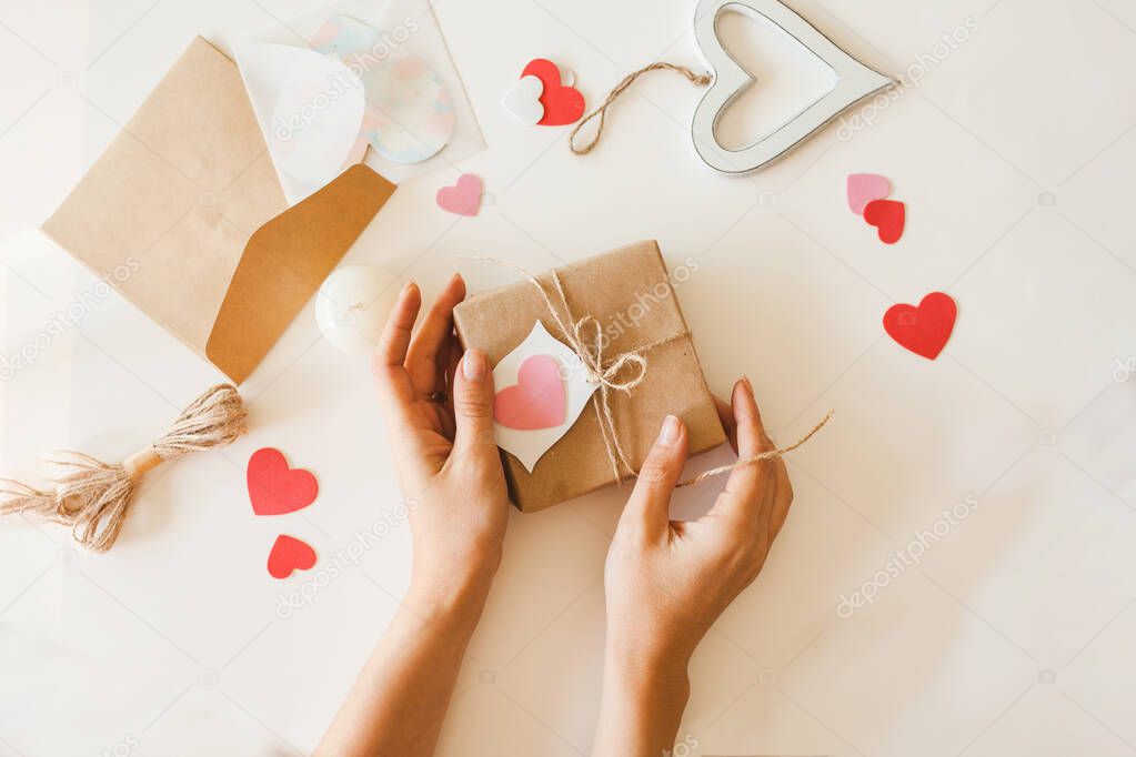 Female wrapping Valentine's day presents in brown paper with jute rope and paper hearts.