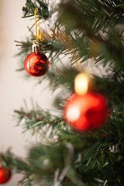 Yeşil dalda kırmızı yuvarlak Noel ağacı süsü ve arka planda tel lambaları var. Kış tatili tebrik kartı. Noel ağacı süslenmiş, yakın plan.