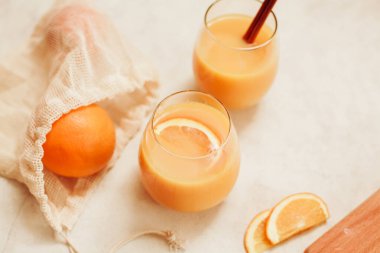 Portakal suyu. Cam bardaklı, paslanmaz çelik pipetli ve beyaz masa üzerindeki tahta kesme tahtalı portakallar.