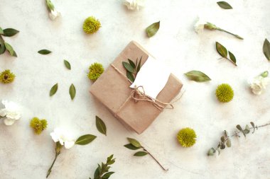 Bahar tatili çiçekli arka plan - kahverengi kağıda sarılı beyaz arka plan hediye, yeşil kasımpatı, beyaz karanfil ve okaliptüs yaprakları.