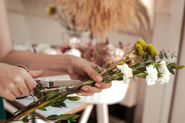 Çiçek buketini beyaz karanfiller, okaliptüs yaprakları ve yeşil kasımpatı ile düzenleyen genç bir kadın. Çiçekçi. Sapları nasıl keseceğini ve çiçekleri nasıl düzenleyeceğini.
