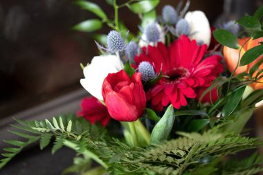 Kış düğün buketi - kırmızı kasımpatı, turuncu laleler, mavi devedikeni ve eğreltiotu yaprakları düzenleme.