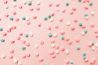 Açık pembe arka planda pembe, beyaz ve mavi yıldız şekilli serpinti. Pembe arka planda renkli yenilebilir pasta süslemesi.