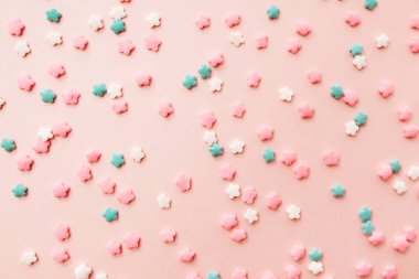 Açık pembe arka planda pembe, beyaz ve mavi yıldız şekilli serpinti. Pembe arka planda renkli yenilebilir pasta süslemesi.