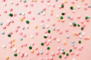 Açık pembe arka planda pembe, beyaz, sarı, mavi ve yeşil yıldız şekilli serpinti. Pembe arka planda renkli yenilebilir pasta süslemesi.