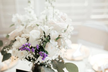 MOdern düğün dekoru - beyaz masa örtülü misafir masaları, altın tabaklar, beyaz güller ve okaliptüs çiçekli yapraklar.