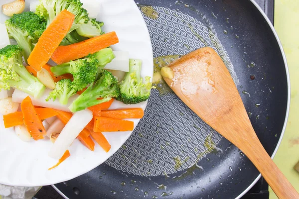 Szakács keverjük megsütjük brokkoli, sárgarépa és petrezselyemgyökér, a serpenyőben — Stock Fotó