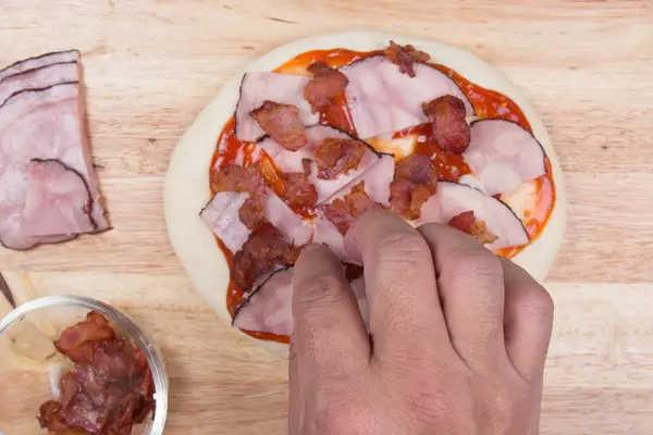 Putting Bacon on pizza crust — Stock Photo, Image