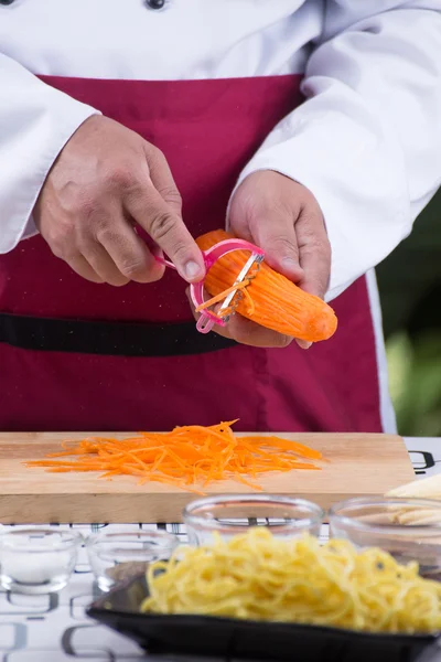 Koch schneidet Karotten mit Schäler in Scheiben — Stockfoto