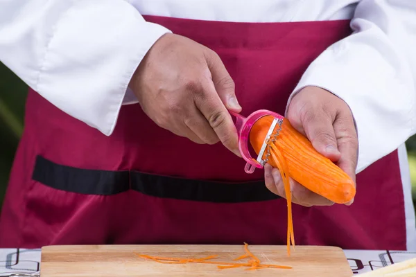 Koch schneidet Karotten mit Schäler in Scheiben — Stockfoto