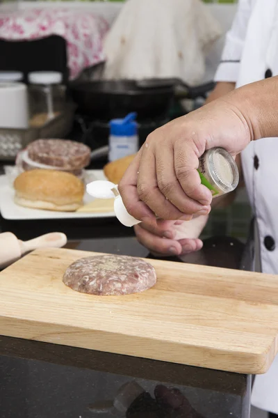 Chef colocando pimenta no hambúrguer de carne — Fotografia de Stock