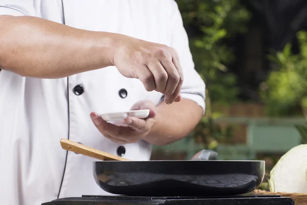 Шеф-повар выкладывает соль на сковородку для приготовления пищи — стоковое фото