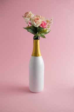 Aşk konsepti. Çiçek buketi pembe arka planda bir şişe şampanya..