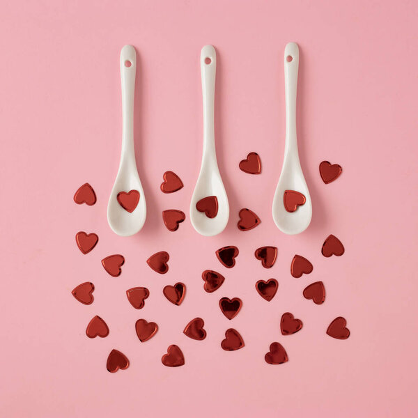 Creative composition with red hearts and white spoons on a pink background. Valentines or woman's day background. Minimal flat lay.