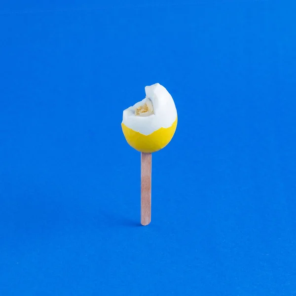 Yellow eggs bitten on a stick like ice cream on a blue background. Minimal creative concept of Easter or food.