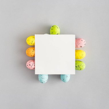 Renkli Paskalya yumurtaları ve gri arka planda kağıt kartı olan yaratıcı bir kompozisyon. Minimal bahar tatili konsepti. Yaratıcı kopyalama alanı. Düz yatıyordu.