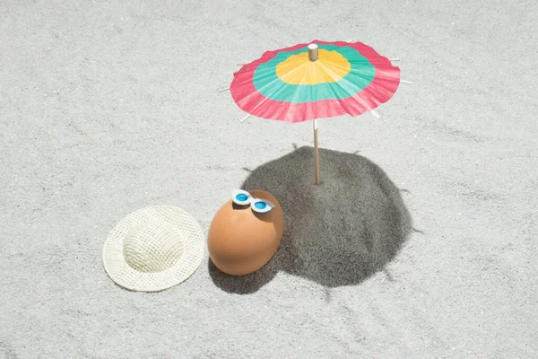 Creative Easter composition with egg, hat and beach umbrella on the sand. Summer and holiday background  idea. Flat lay.