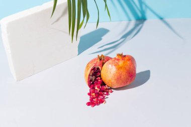 Taze nar, beyaz mermer taş ve mavi ve gri arkaplanlı palmiye dallı yaratıcı bir yaz kompozisyonu. Asgari taze doğa ya da gıda konsepti.