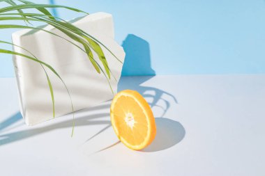 Yaratıcı bir yaz kompozisyonu. Taze turuncu, beyaz mermer bir taş dilimi ve mavi ve gri arka planda bir palmiye dalı. Asgari taze doğa ya da gıda konsepti.