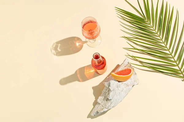 Creative summer background with a fresh cocktails, a glass, a piece of grapefruit, a sea stone and a green palm branch. Summer, tropical, fresh cocktail concept. Flat lay.