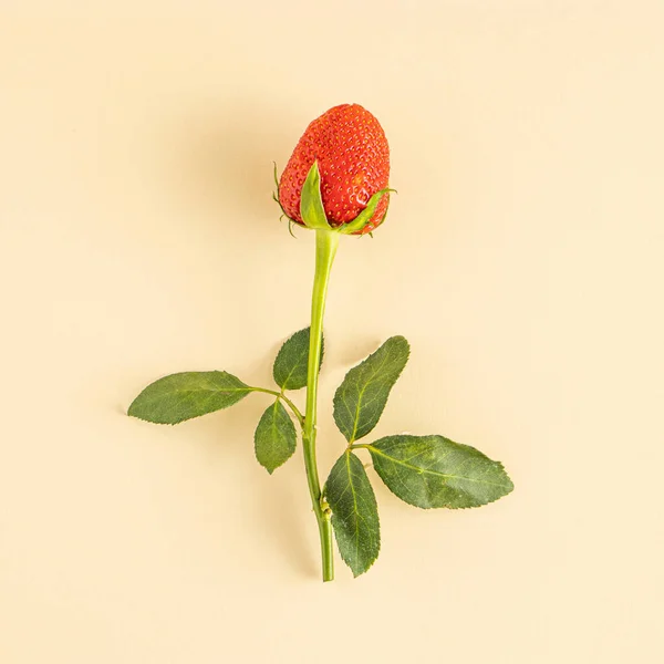 Creative composition with strawberry and green leaves of rose flower on a pastel beige background. Minimal food or love concept. Flat lay.