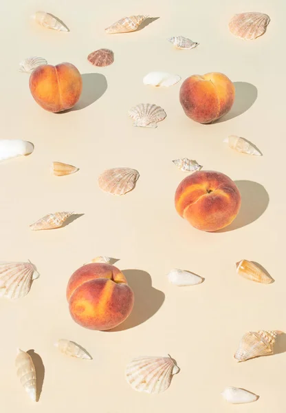 Creative summer concept with shells, fresh peaches and paper card note against pastel beige background. Minimal beach vacation or healthy food layout.